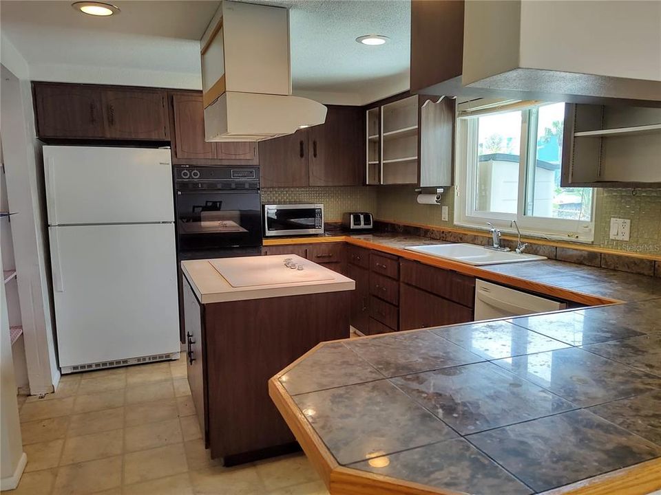 Kitchen has tile counters, cooktop cooking island, built in stove, dishwasher (2019) microwave, refrigerator, and tons of cabinet space and large pantry.
