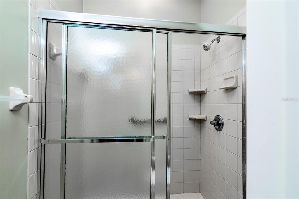 The shower in the master bath has glass doors, grab bar and ceramic tile surround.