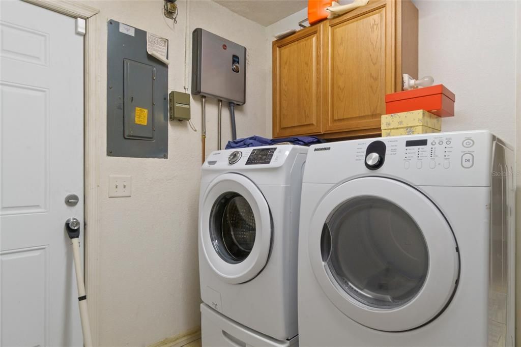 The Inside Laundry Room has a Tankless Hot Water Heater on the Wall next to the Cabinets. The Door to the left of the Electrical Panel is a Door to Outside
