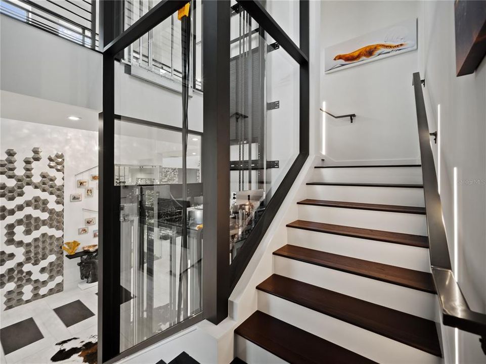 The custom framed glass elevator creates a remarkable centerpiece for the stairs, illuminated by inlaid wall lighting.