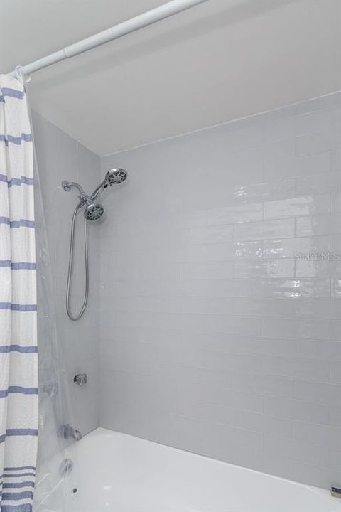 The shower with tub has dual shower heads and gray tile.