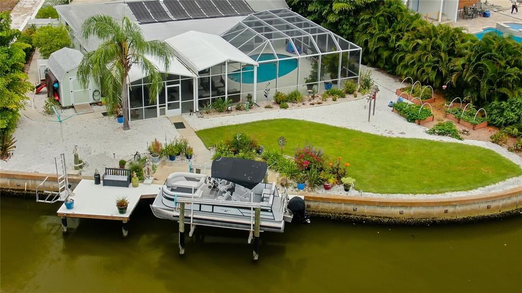 Aerial view of back exterior of house, pool, dock & pontoon boat.