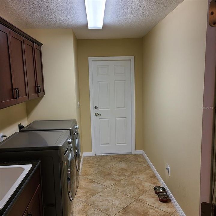 Laundry room with wash sink and extra cabinets door leads to garage