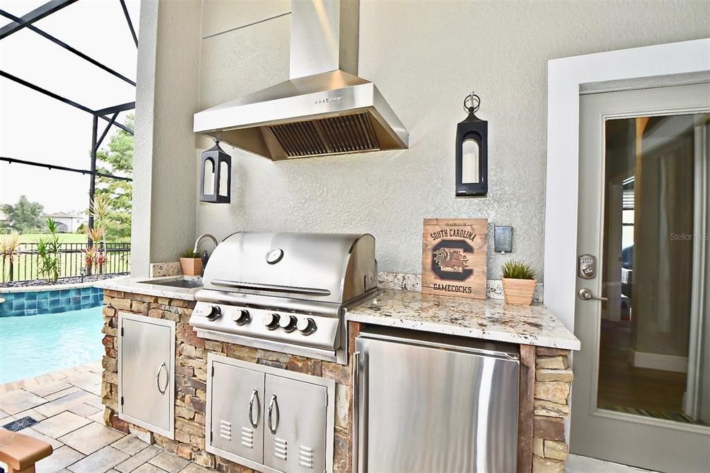 Luxurious Outdoor Summer Kitchen with Granite Countertops, Stainless Grill, & Refrigerator on the Screened in covered Brick Pavered Lanai area with Stunning Custom Pool & Spa equipped with Water Features, Gas Heater & Floor Cleaning System.