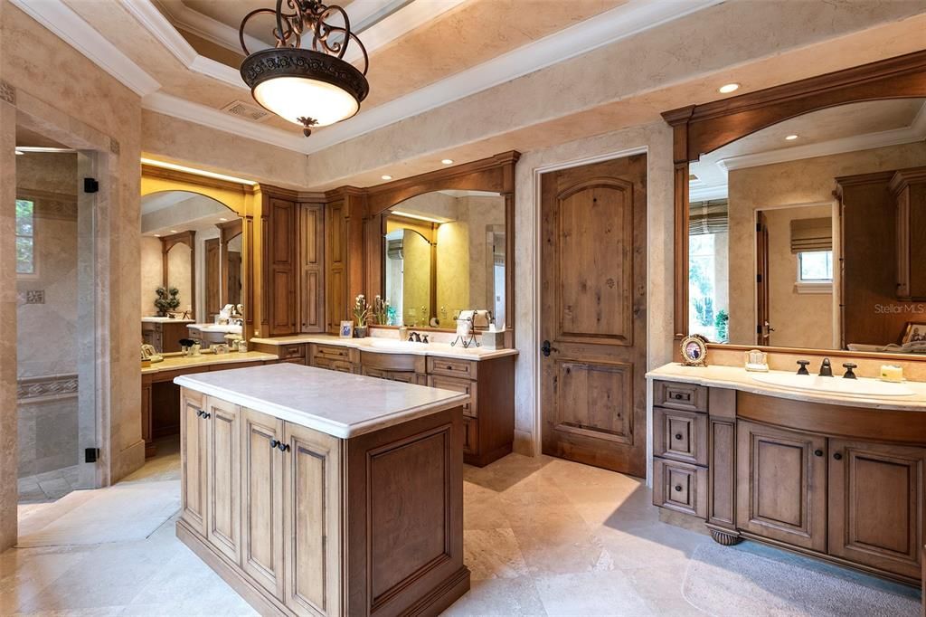 The stunning bath features polished travertine floors, dual vanities, a center island, refrigerator, a walk-in steam shower and separate spa tub.