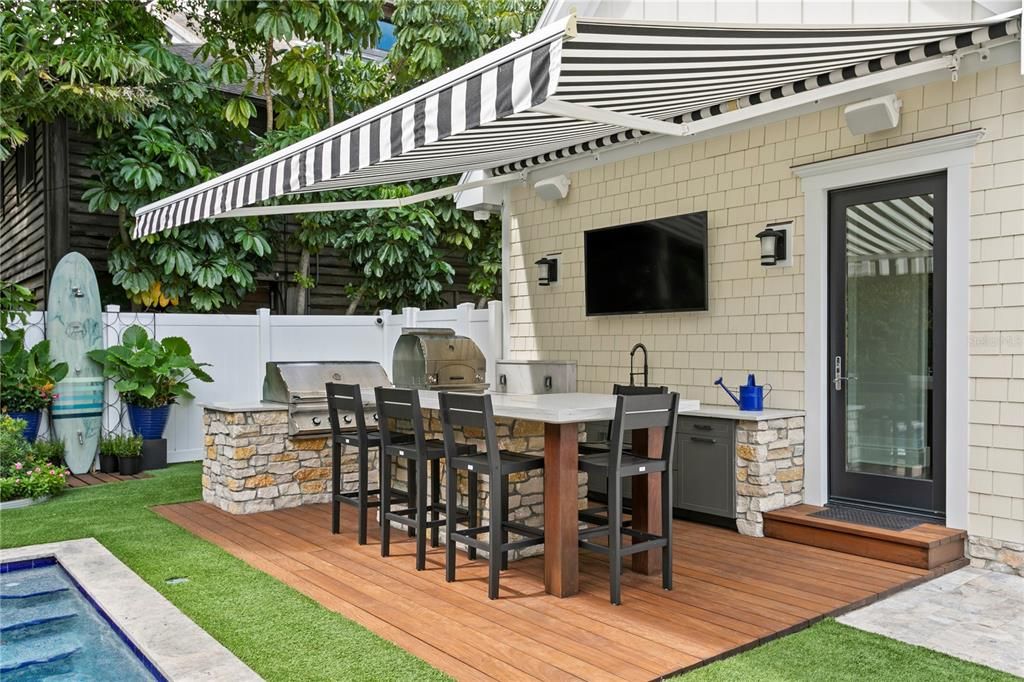 Outdoor chef's kitchen with pizza oven, wet bar, seating for guests with automatic sunshade.