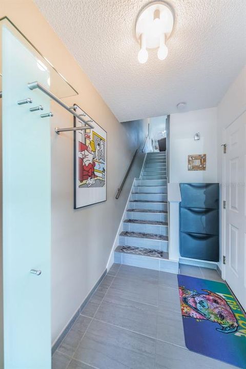 Welcoming foyer with coat rack and shoe caddy. Tiled stairs lead up to 2nd level living area, while door on right leads to garage