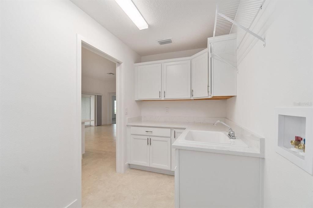 Large inside laundry room with white upper and lower cabinetry with crown molding, utility sink, washer and dryer