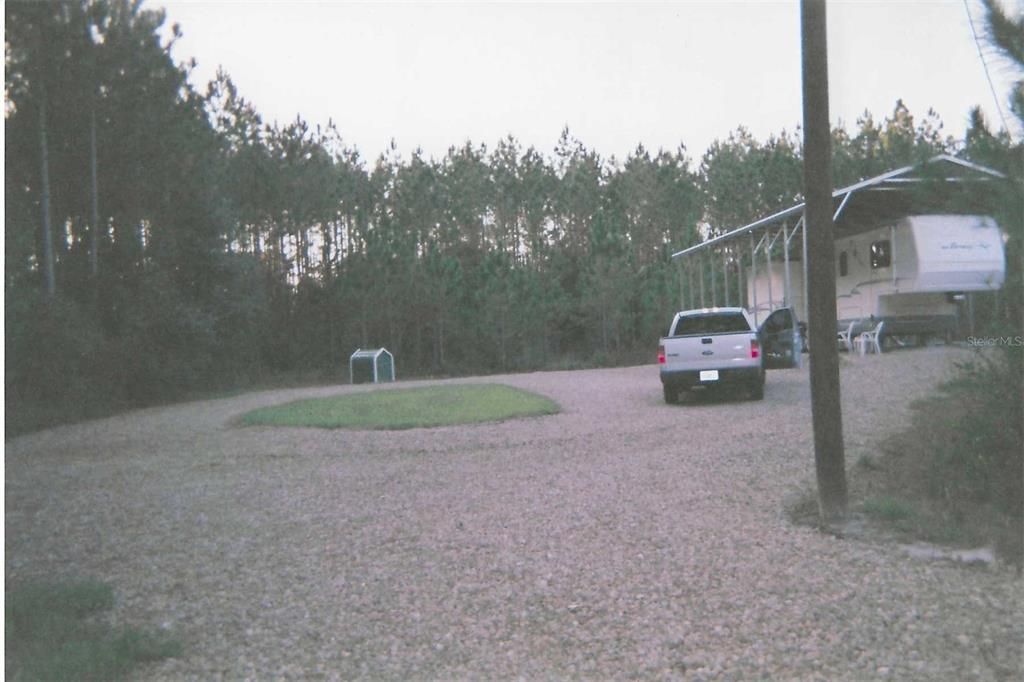 Entry drive, covered RV area, mature pines in background.