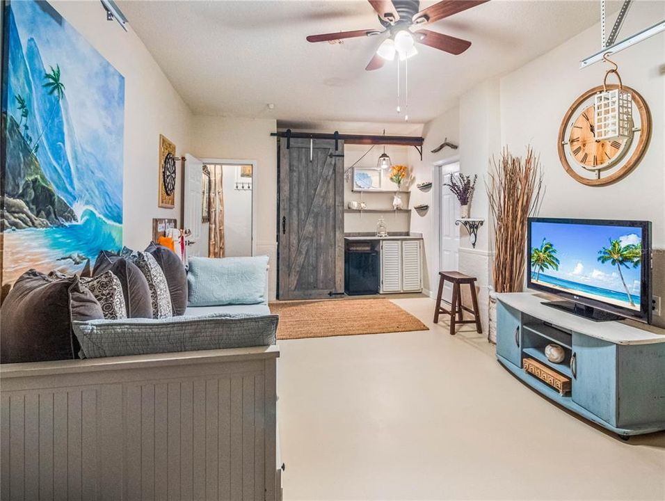 The garage/bonus room has custom barn door, white wood shutter cabinets with stone backsplash and two wood stained shelves above the counter. There is a mini fridge included in the sale. Behind the barn door is a closet rack.