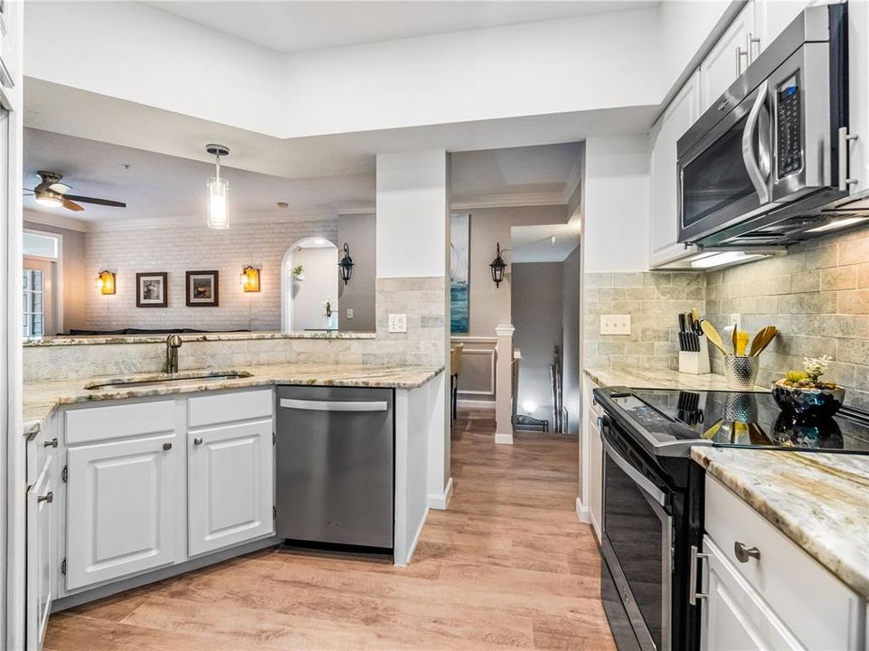 This kitchen is a chef's delight, with granite counters, undermount farmhouse stainless steel sink, granite bar, stainless steel appliances, glass flat top range, built in refrigerator stone backsplash throughout kitchen and flush mount LED lighting.