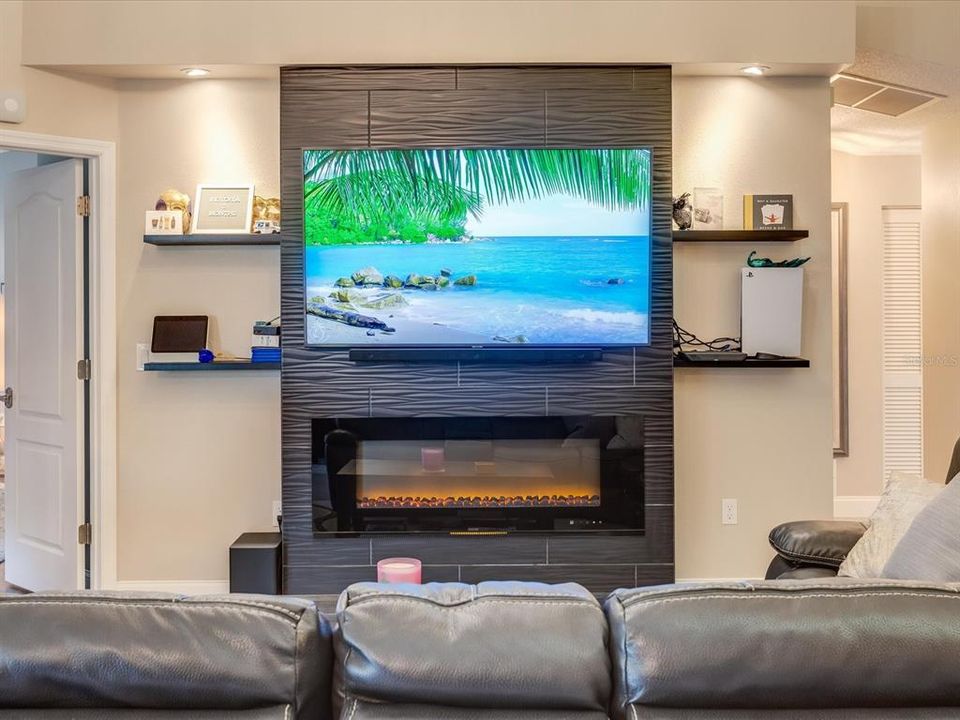 Tiled fireplace wall with spotlights over floating shelves.