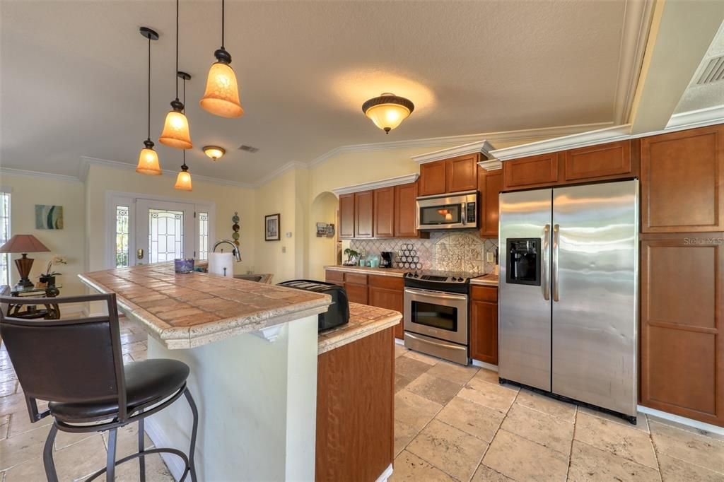 Large open wrap around kitchen with SS appliances, and convenient sit-up bar seating, stone backsplash with mosaic behind stove, stone tile countertops, with solid wood cabinetry with crown molding