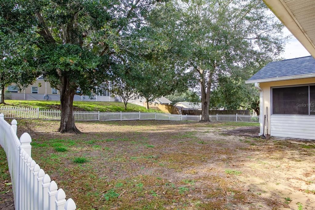 Large side and back yard with small white picket fence and an abundance of shade from large oak trees.