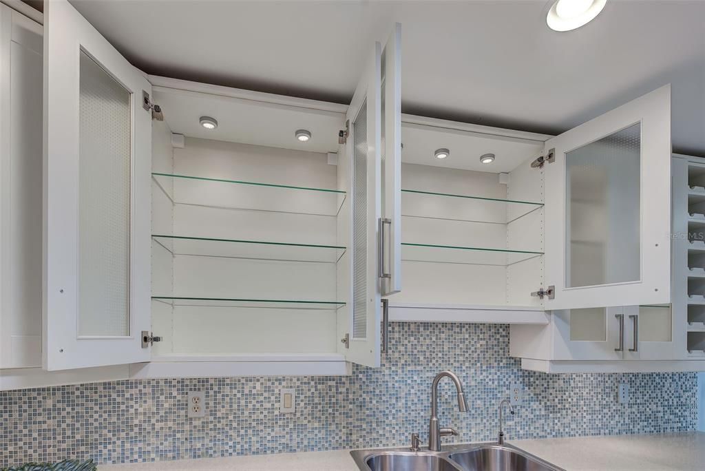 Custom lit white wood cabinetry with glass shelving.