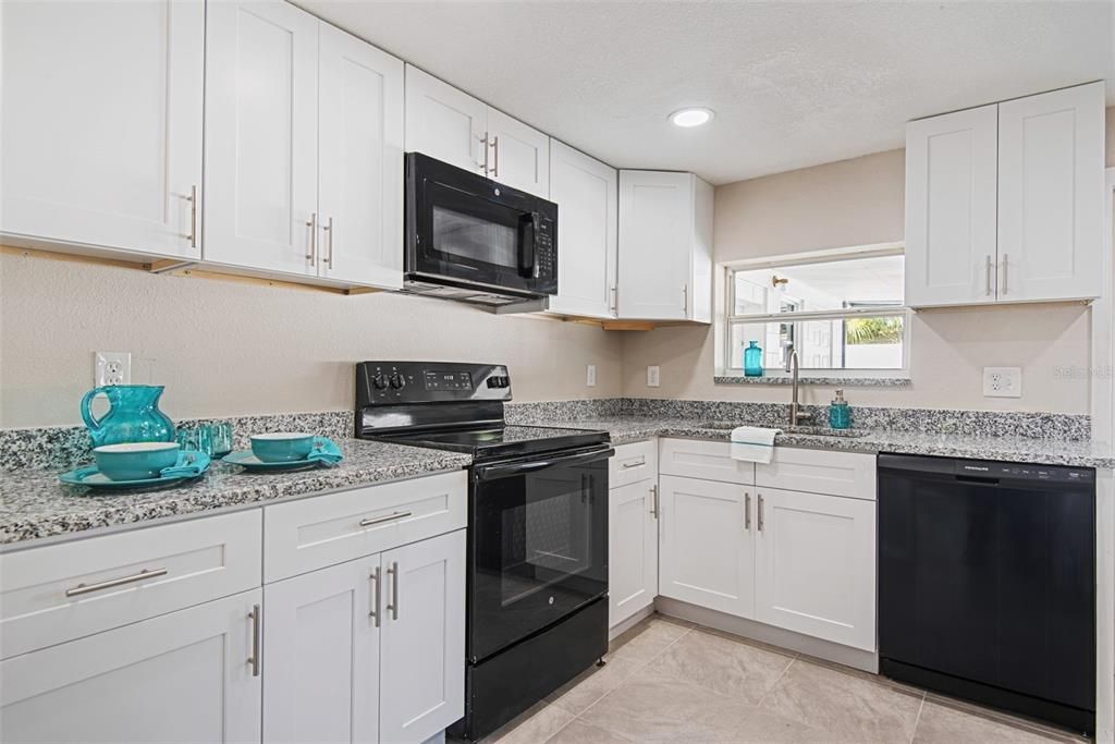 The dining area leads to a brand new kitchen with granite counters, White and bright and fresh. The kitchen window overlooks the patio area. Matching black appliances. New refrigerator, microwave, and dishwasher. New cupboards, hardware, flooring, and canned ceiling lights!