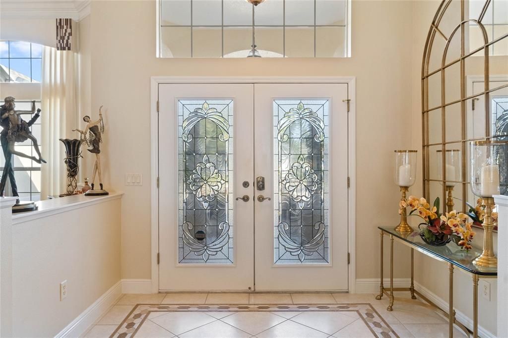 Double leaded glass front doors open into an inlaid tiled entry floor flanked by round columns.