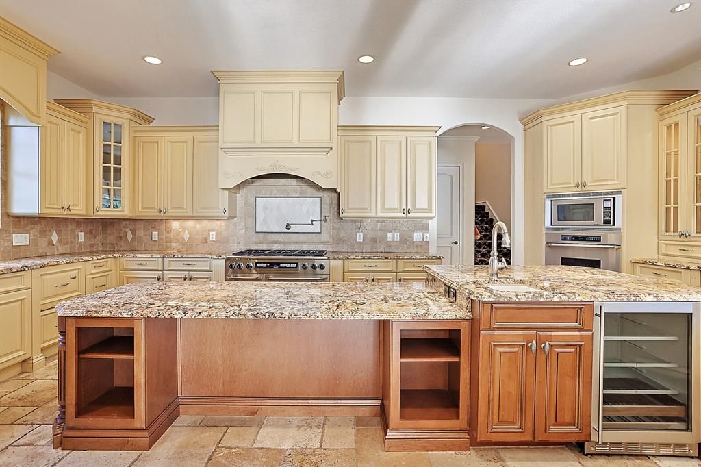 The well-appointed kitchen is complete with custom wood cabinetry, granite counters, commercial-grade appliances, including a gas range, prep island with storage and extra sink