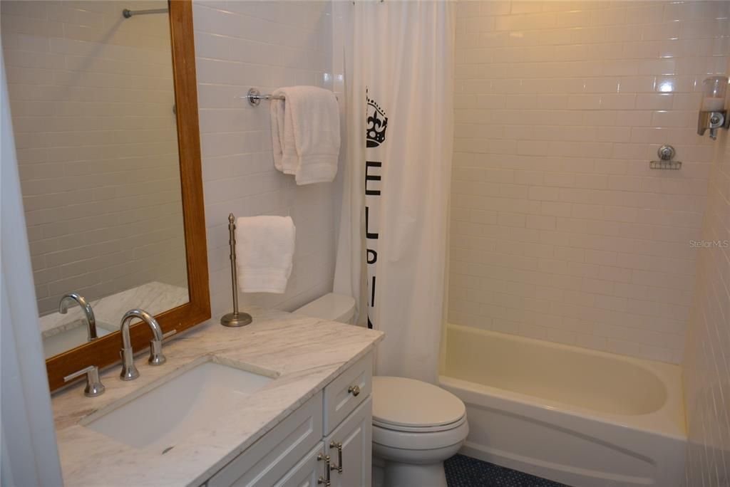 Renovated guest bathroom with exterior barn door, floor-to-ceiling white subway tile, crown molding, undermount sink with cultured marble  countertops and penny tile floors