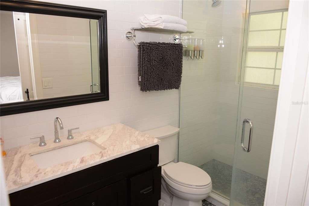 Master bath with floor-to-ceiling white subway tile, open glass shelving, glass step-in shower,  crown molding and spacious vanity with cultured marble countertop & undermount sink and exterior barn door