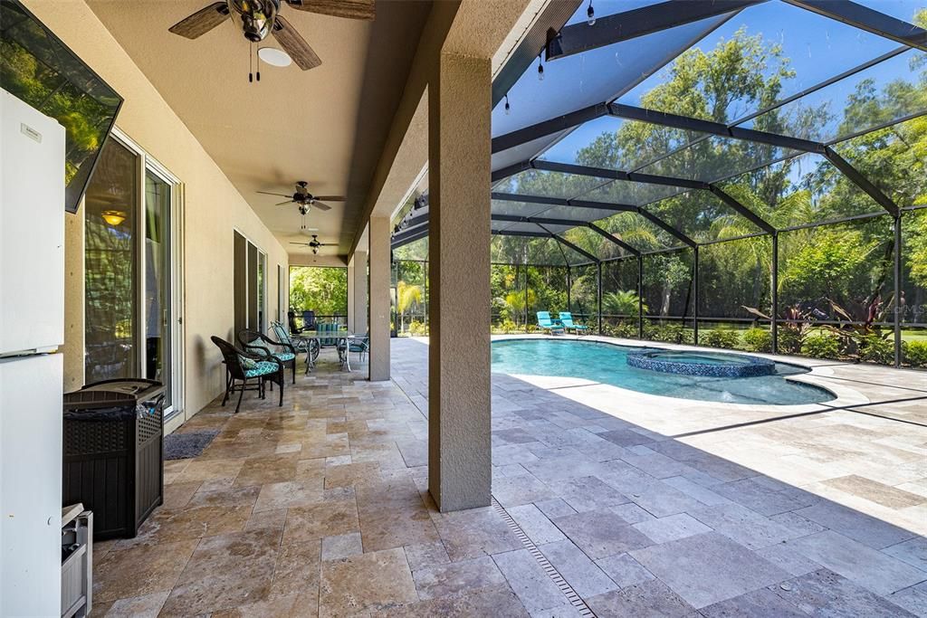 Travertine pavers surround a large and inviting pool with lots of covered seating along the entire width of the house.