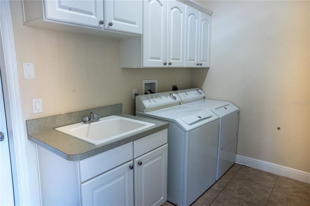 A dream utility room with a walk-in storage closet, laundry tub, upgraded Maytag Washer & Dryer, additional cabinets on other side of room (not shown), tile floors. door to garage.