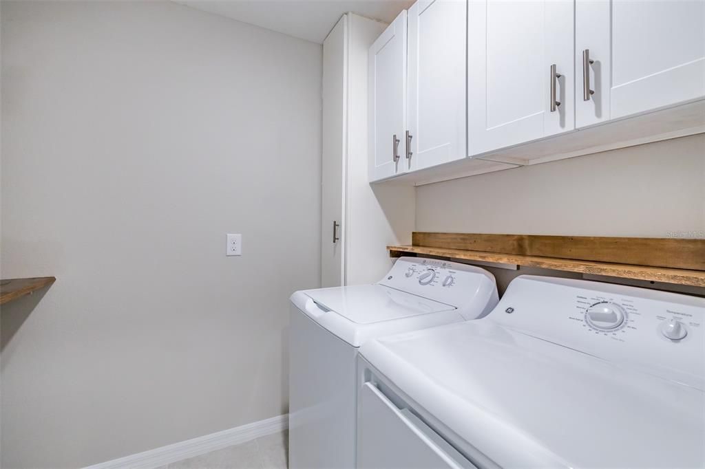 Laundry room features wood shelving and enclosed cabinets. GE Washer/Dryer are included.