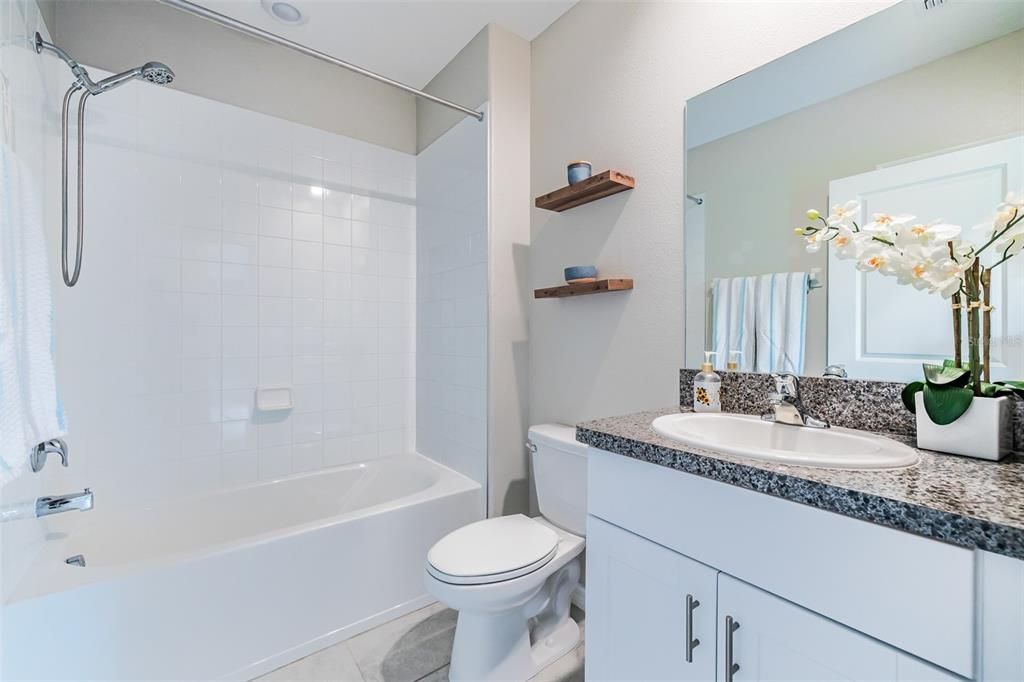 The downstairs bathroom features a shower/tub combo with handheld shower head, floating wood shelves and white cabinets.