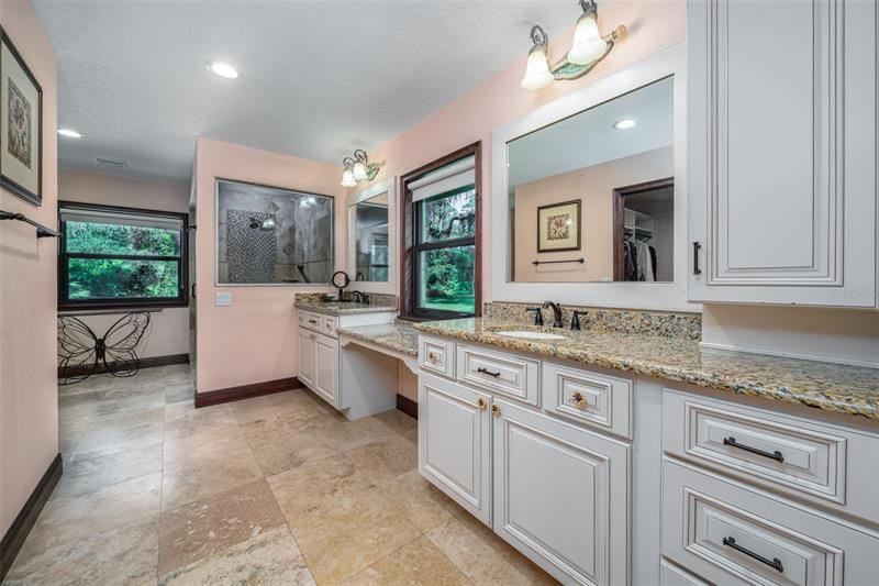 Primary bath with travertine floors, dual sinks, area to sit down for make-up with large windows for natural lighting.