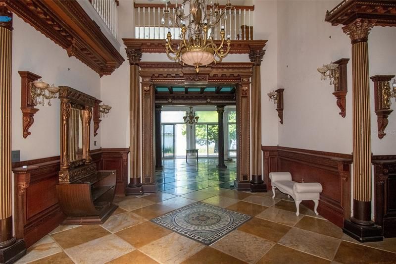 Grand front entry foyer, carved wood, pillars and diagonally laid flooring with medallion inlay.
