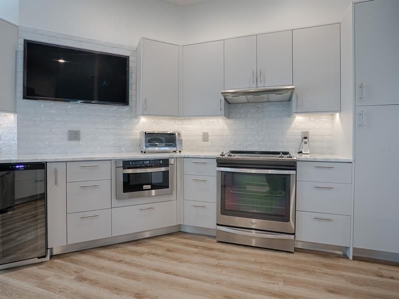 THE GLASS BACKSPLASH GOES UP THE WALL BEHIND THE MOUNTED TV.  CONVENIENT UNDER COUNTER MICROWAVE WITH A STAINLESS VENT OVER THE BUILT-IN, SMOOTH TOP ELECTRIC STOVE.
