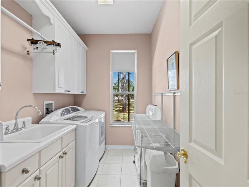 Inside Laundry Room with Sink, Base Cabinets, Clothes Hanging Rod, 42" Upper Cabinets, and Window Looking Out to the Backyard Area