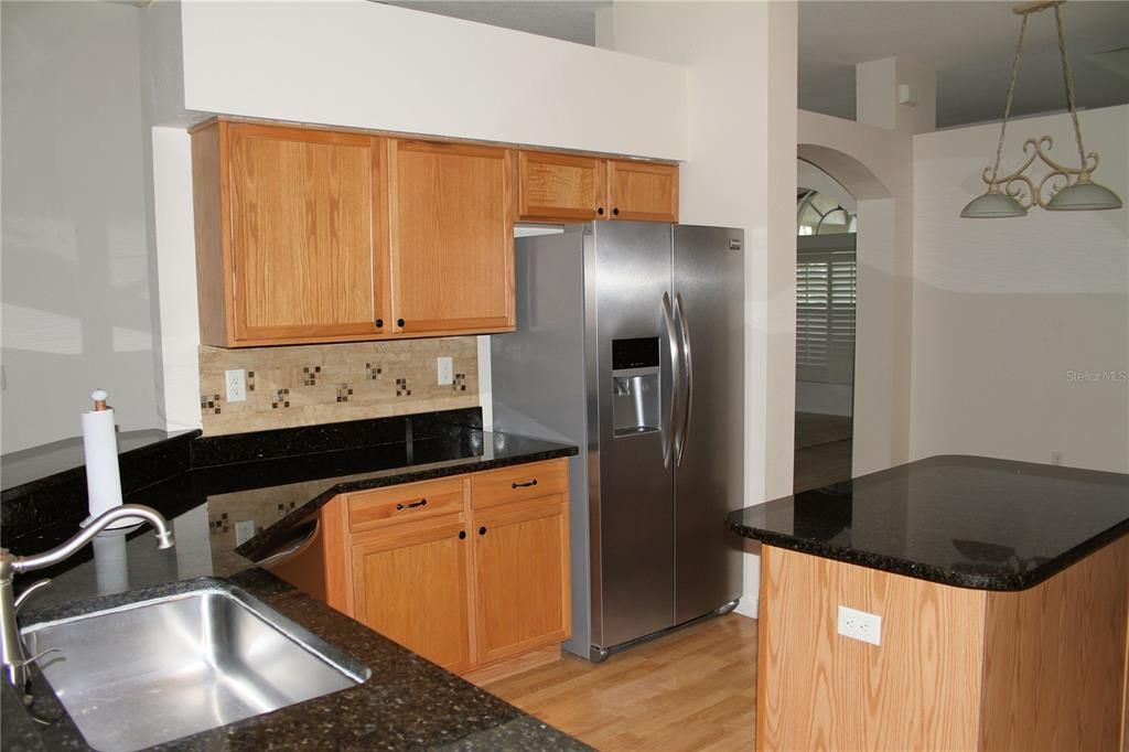 Modern kitchen with wood cabinets, stainless steel appliances tiled backsplash and granite counters.