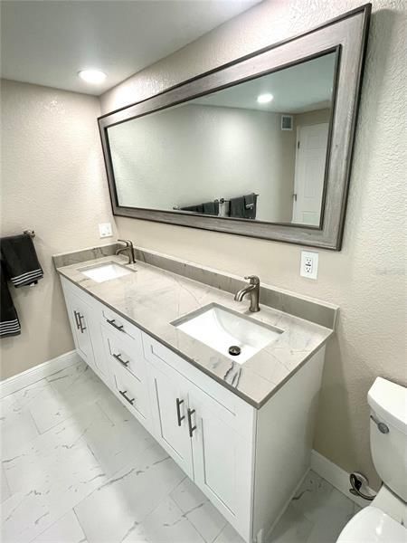 Double sinks with beautiful cabinetry and ceramic tile flooring that looks like Carrara marble.