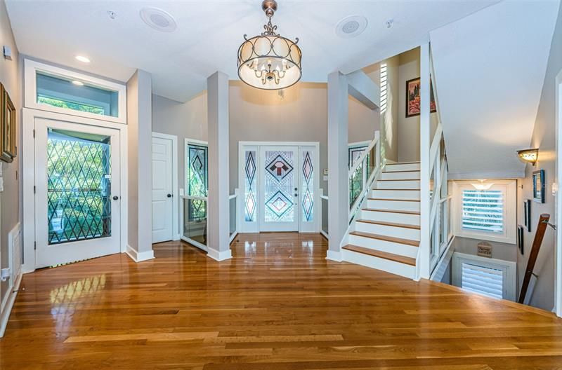 Stunning foyer featuring hardwood flooring, stained glass door and windows, elevator and stair access to other floors.