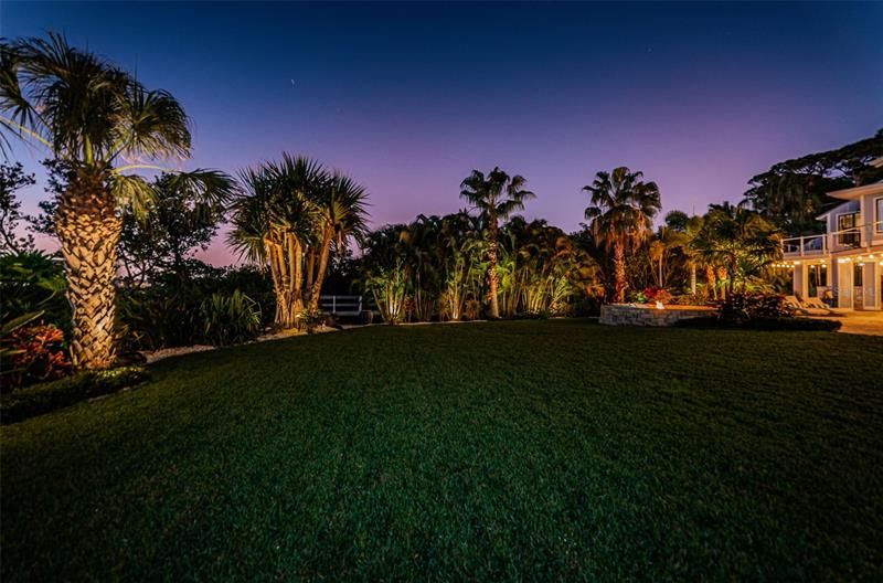 Lush, tropical landscaping surrounds the velvety lawn, with accent lights.