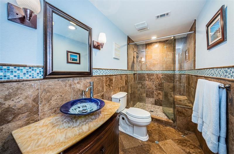 Bathroom with glass vessel sink and walk-in shower with bench.