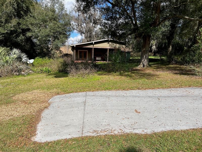 A concrete parking pad in front of the home at the end of a tree-lined driveway.