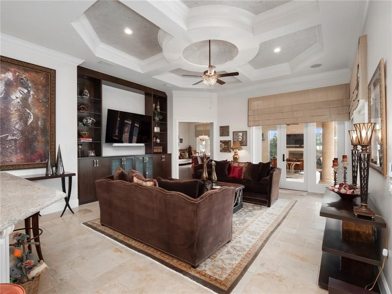 The fabulous family room boasts a detailed ceiling and custom built-in that surrounds the TV with elegant glass display shelves and plenty of cabinet storage.