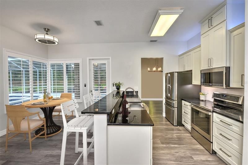 Eat-in kitchen with door to lanai, plantation shutters, breakfast quartz bar and counter, custom stainless steel sink, and stainless steel appliances.