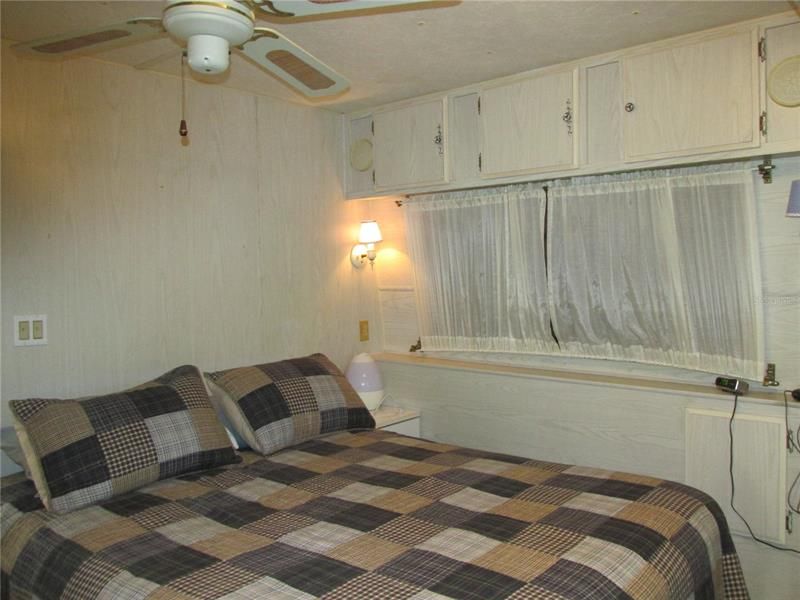 Bedroom has a queen size bed, ceiling fan and overhead storage cabinets.