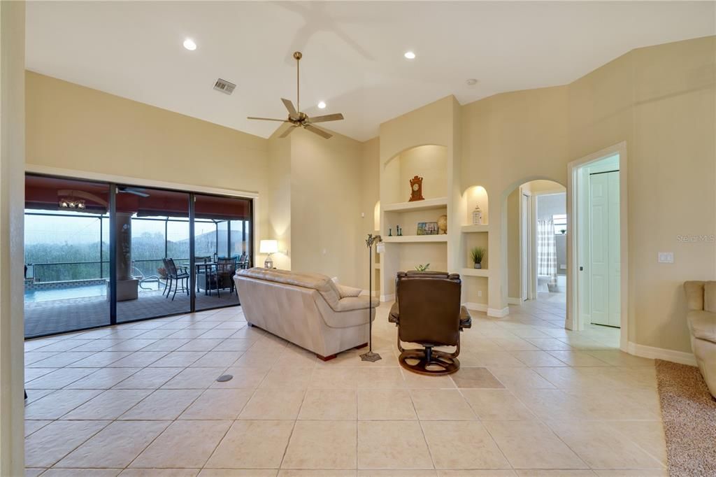 Great room with built in shelving, cathedral ceiling, and wide sliders leading to large paver lanai overlooking the canal