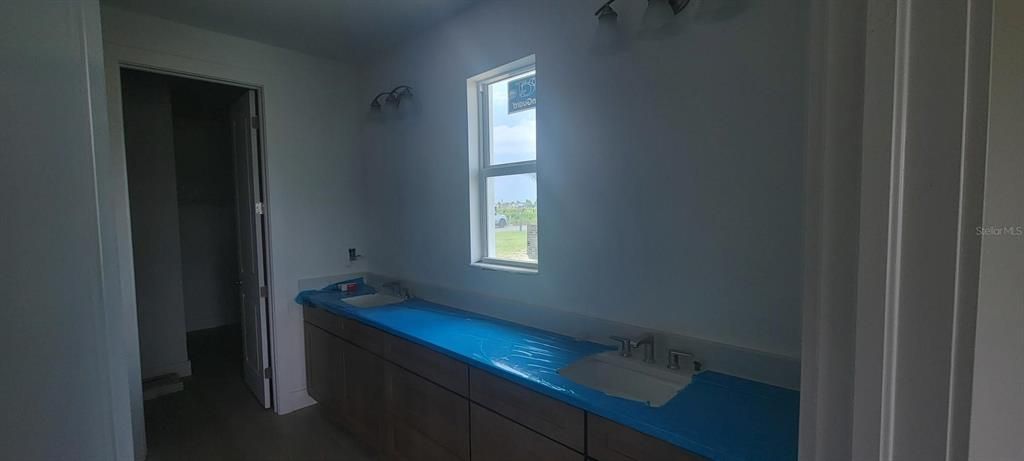 Primary bathroom with dual-sinks and double walk-in closet off the the left (Countertops protected by blue cover)