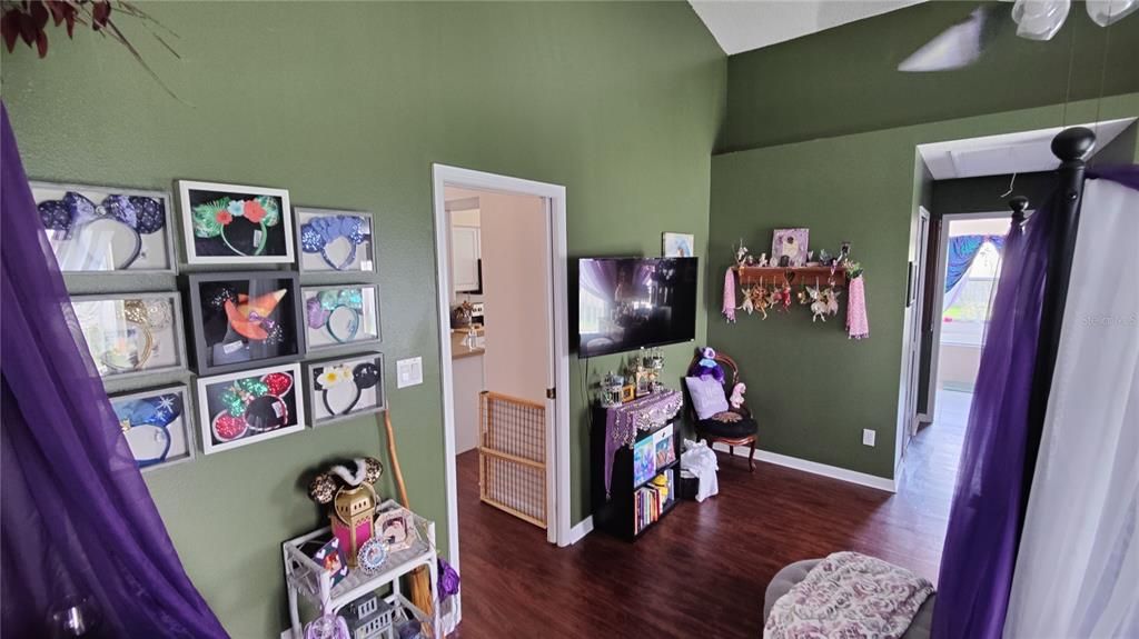 Master bedroom has a decorative display shelf on one wall and cathedral ceilingce saving pocket door leads to great room