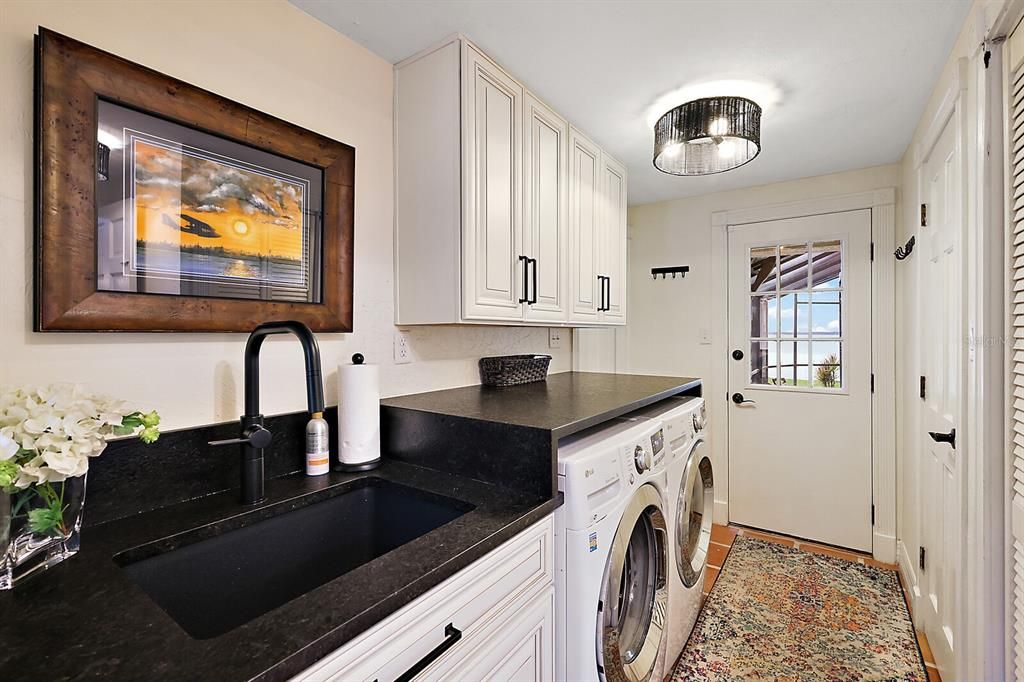 Utility room with Leathered granite, a deep sink and lots of cabinetry. Door to pool and 1/2 bath. Garage access to the left