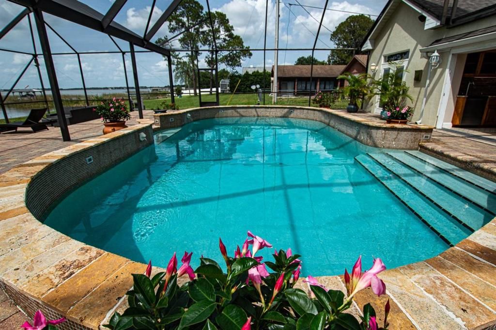 The spacious pool lanai has a grilling area with a sink, outdoor table with seating for six and a sofa and two chaise lounge chairs.