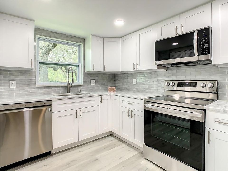 The Well-equipped Kitchen with upgraded LG stainless-steel appliances, including a convection oven with air fryer, soft close cabinets, designer marble countertops extended for a convenient breakfast bar, a stylish glass tile backsplash, an upgraded Kohler faucet, can lighting, and a spacious pantry