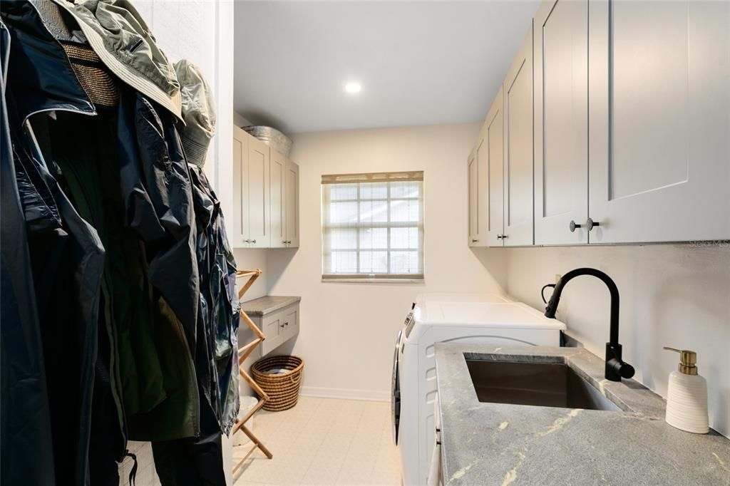 The spacious laundry room offers practicality and organization with a sink, counter, and cabinets.