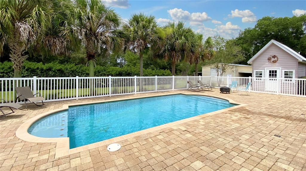 Fenced saltwater pool with cabana and firepit. Palm trees line pool for privacy.