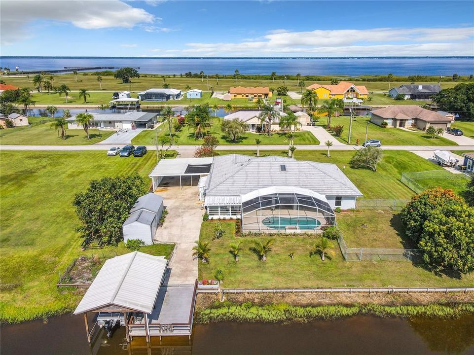 Aerial view of the back of the home, showing the boat dock, sheds, pool, lanai and home.  In the background of the picture shows Lake Walk-In-Water.